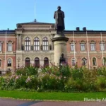 The image depicts a grand building at Uppsala University, showcasing classic architectural design. The edifice features a symmetrical façade with arched windows on the ground floor and rectangular windows on the upper floors, all framed with decorative moldings.