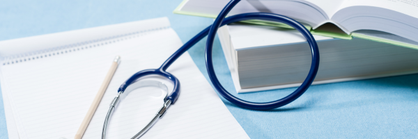The image features a blue stethoscope, an open book with visible pages, a notepad with lined paper, and a pencil.