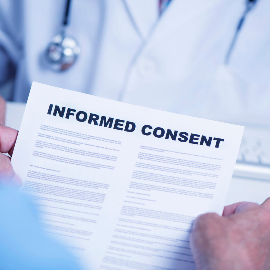 Image shows a close-up of a person holding a document with the bold heading "INFORMED CONSENT." The document has several paragraphs of small, unreadable text.
